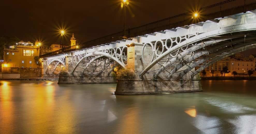 Illuminated river bridge at night in Seville, scenic waterfront