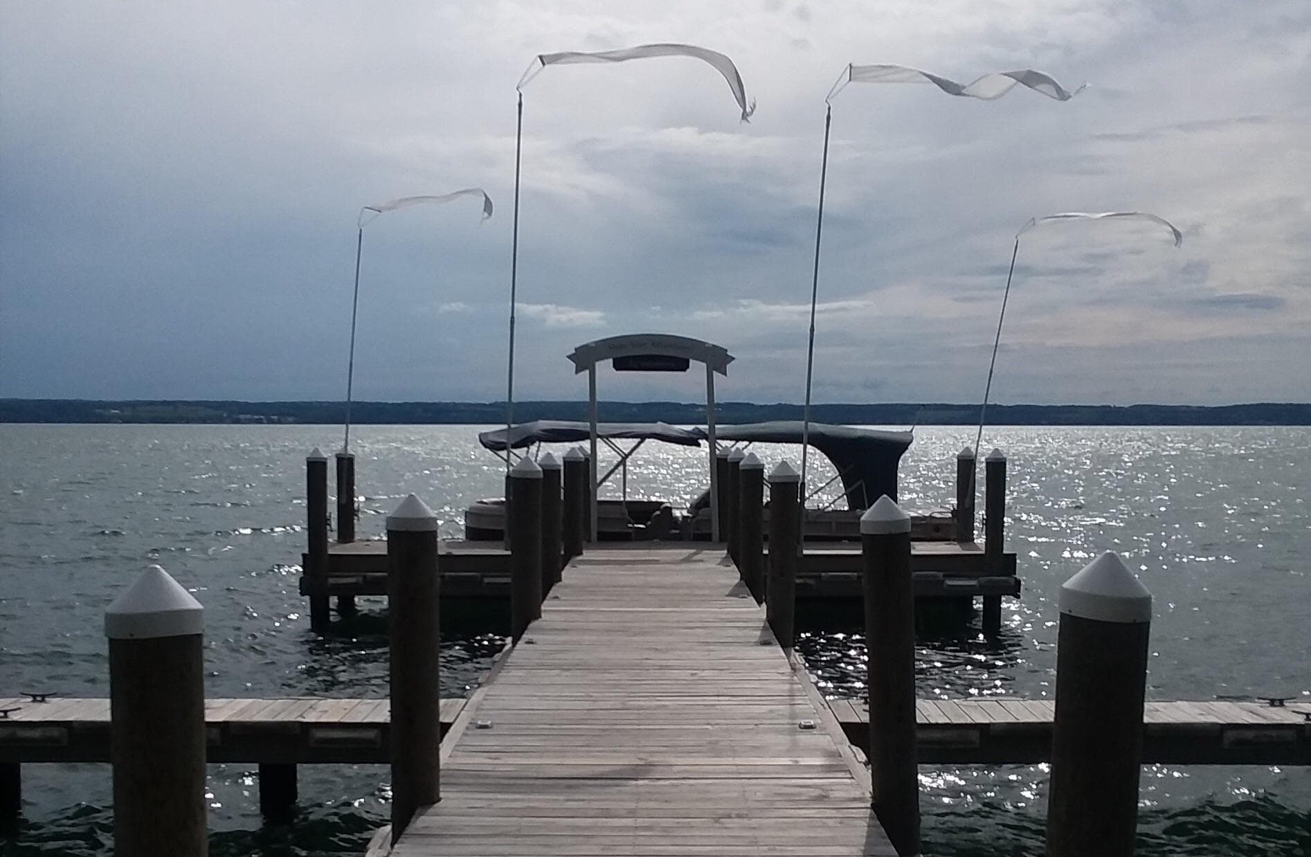 Wooden dock leading to pontoon boat on lake, overcast sky