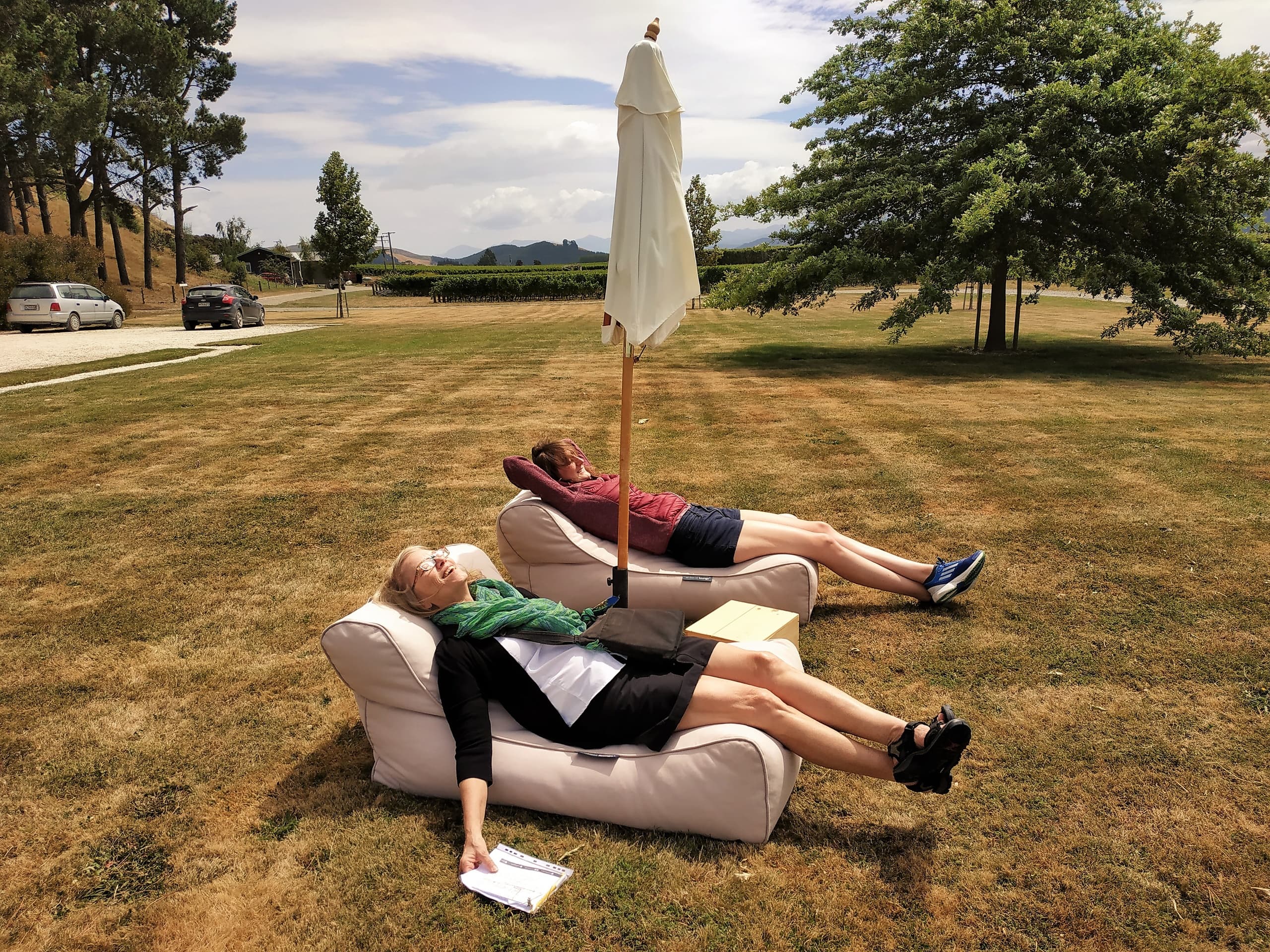 Couple lounging on grassy vineyard lawn under umbrella outdoors