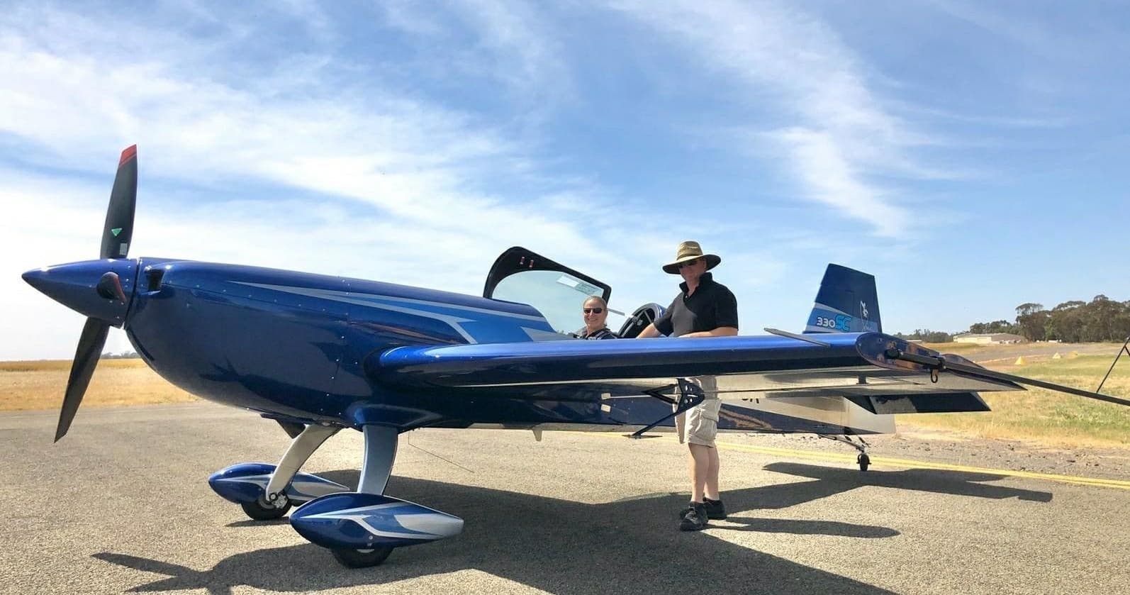 Blue aerobatic plane on sunny airfield with pilot prepping