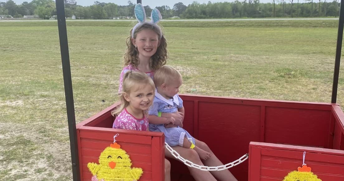 Children riding in red wagon on open grassy field outdoors
