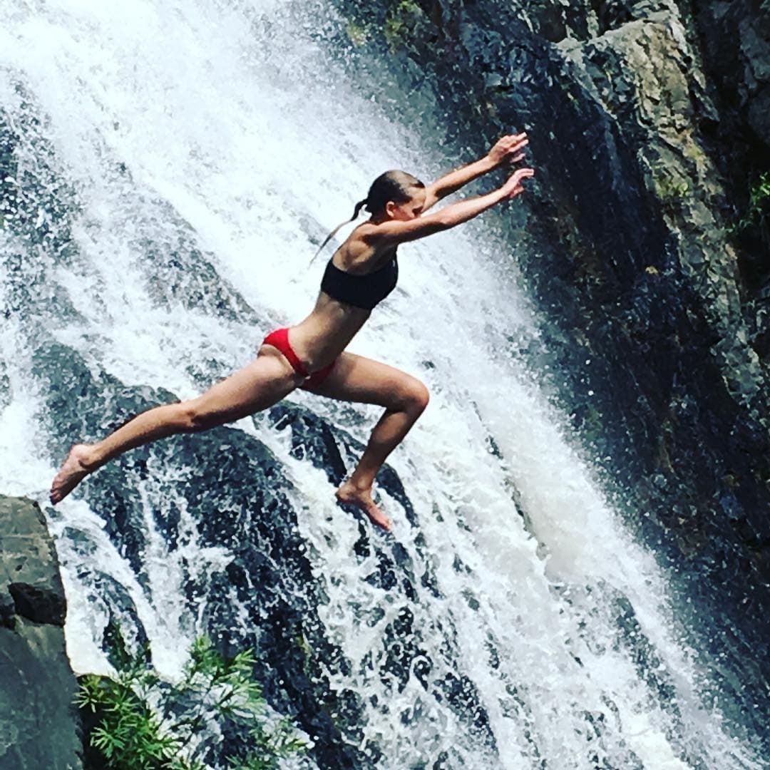 Cliff jumper leaping off waterfall into tropical plunge pool