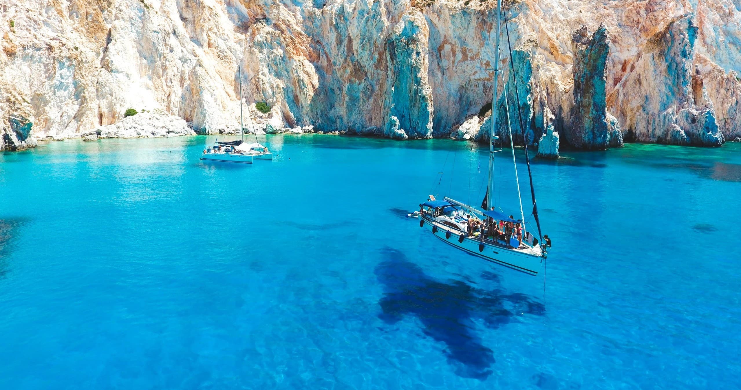 Sailboat anchored in turquoise bay beneath limestone cliffs