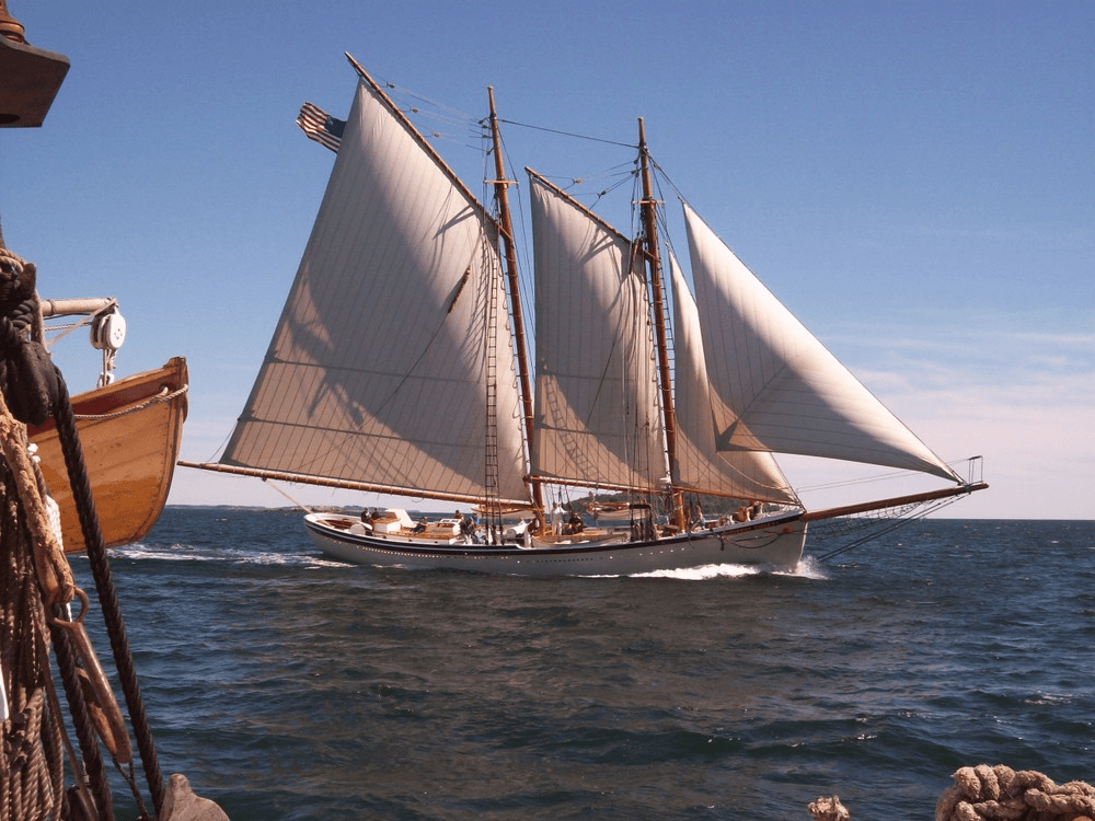 Two-masted schooner under full sail on open ocean, clear sky