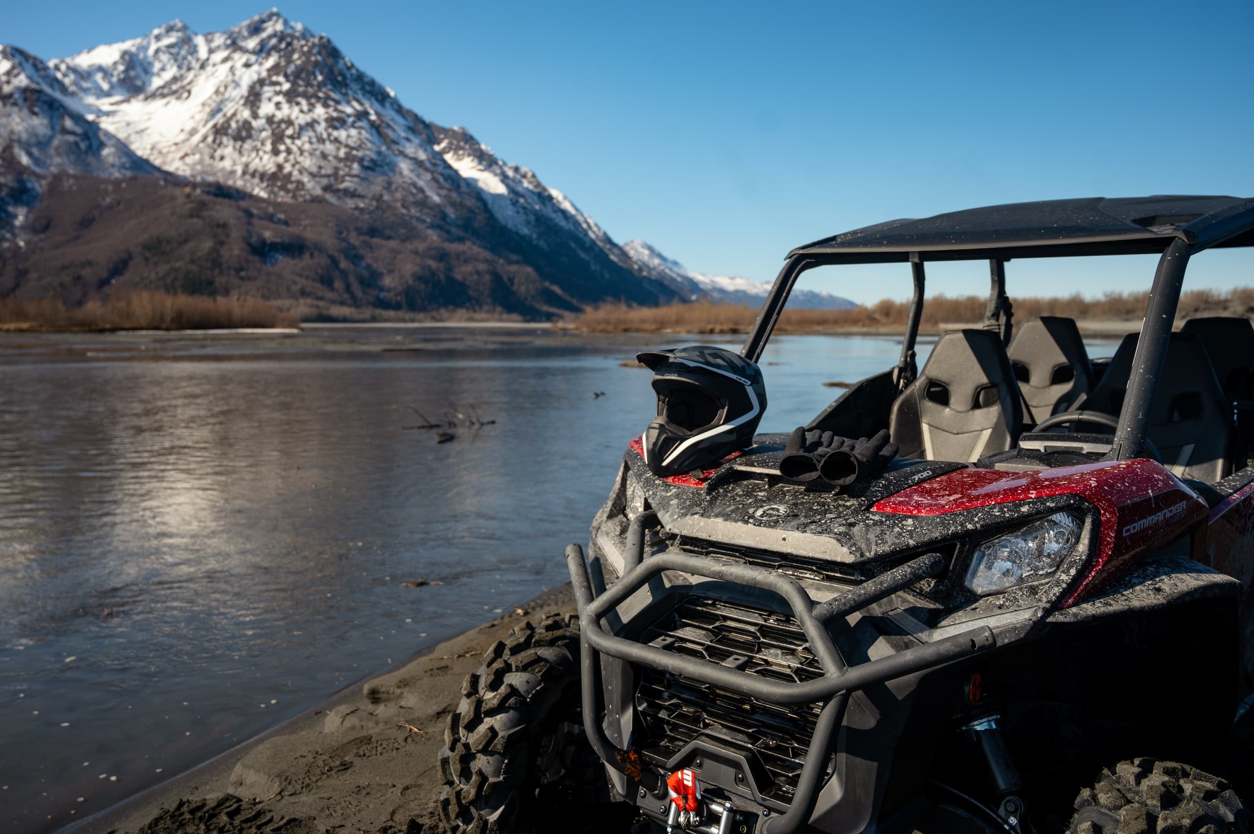 Parked side-by-side UTV beside serene mountain lake and snow peaks