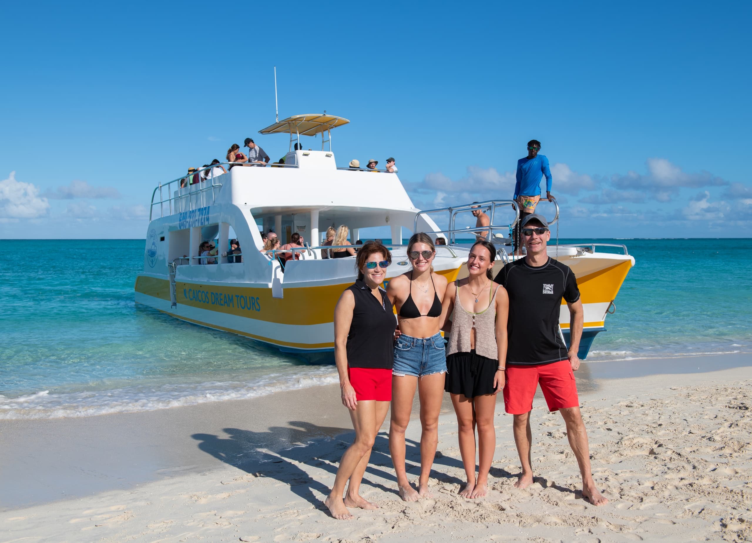 Beachgoers posing in front of yellow tour boat on Caicos white sand