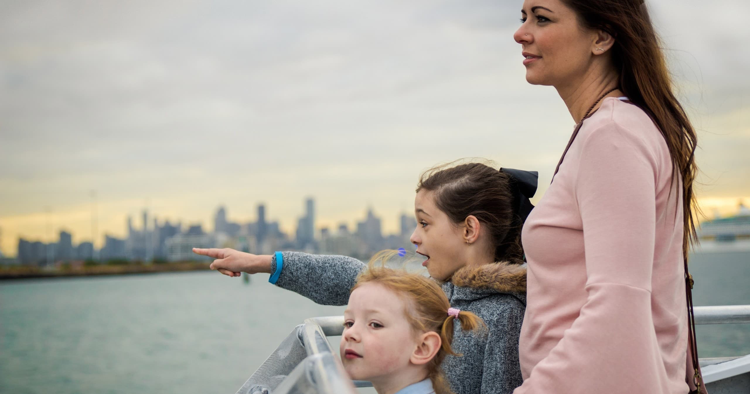 Family on ferry deck pointing toward Melbourne skyline over water