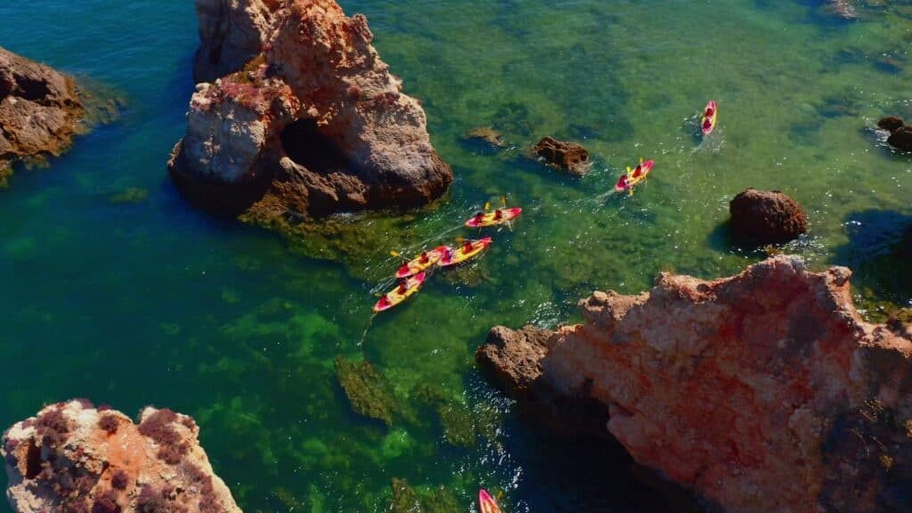 Kayakers paddling among coastal rock formations in clear water