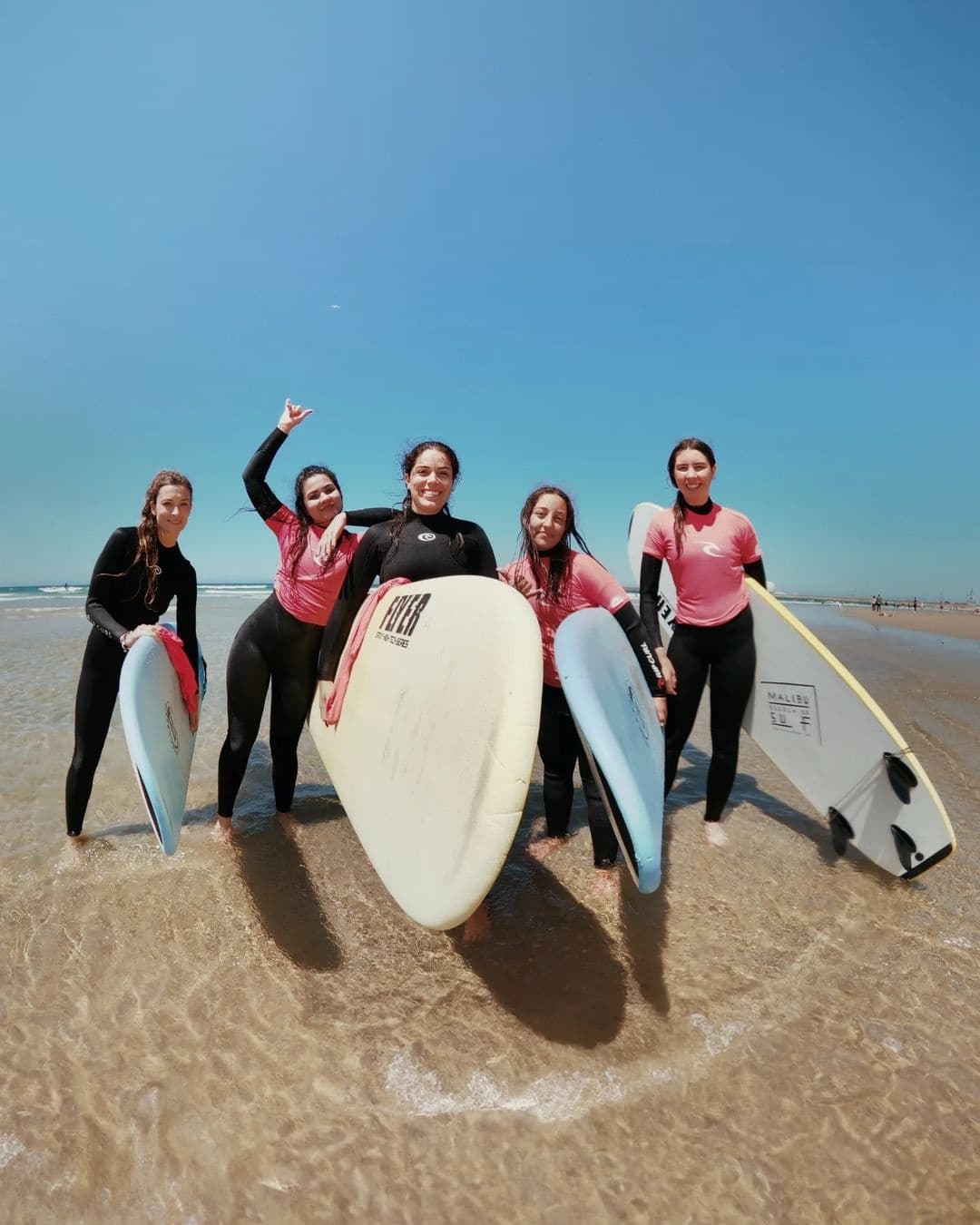 Group surf lesson on sunny sandy beach holding surfboards