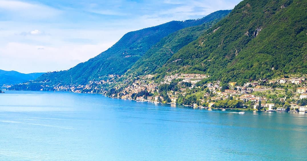 Panoramic alpine lake coastline with mountains and shoreline town