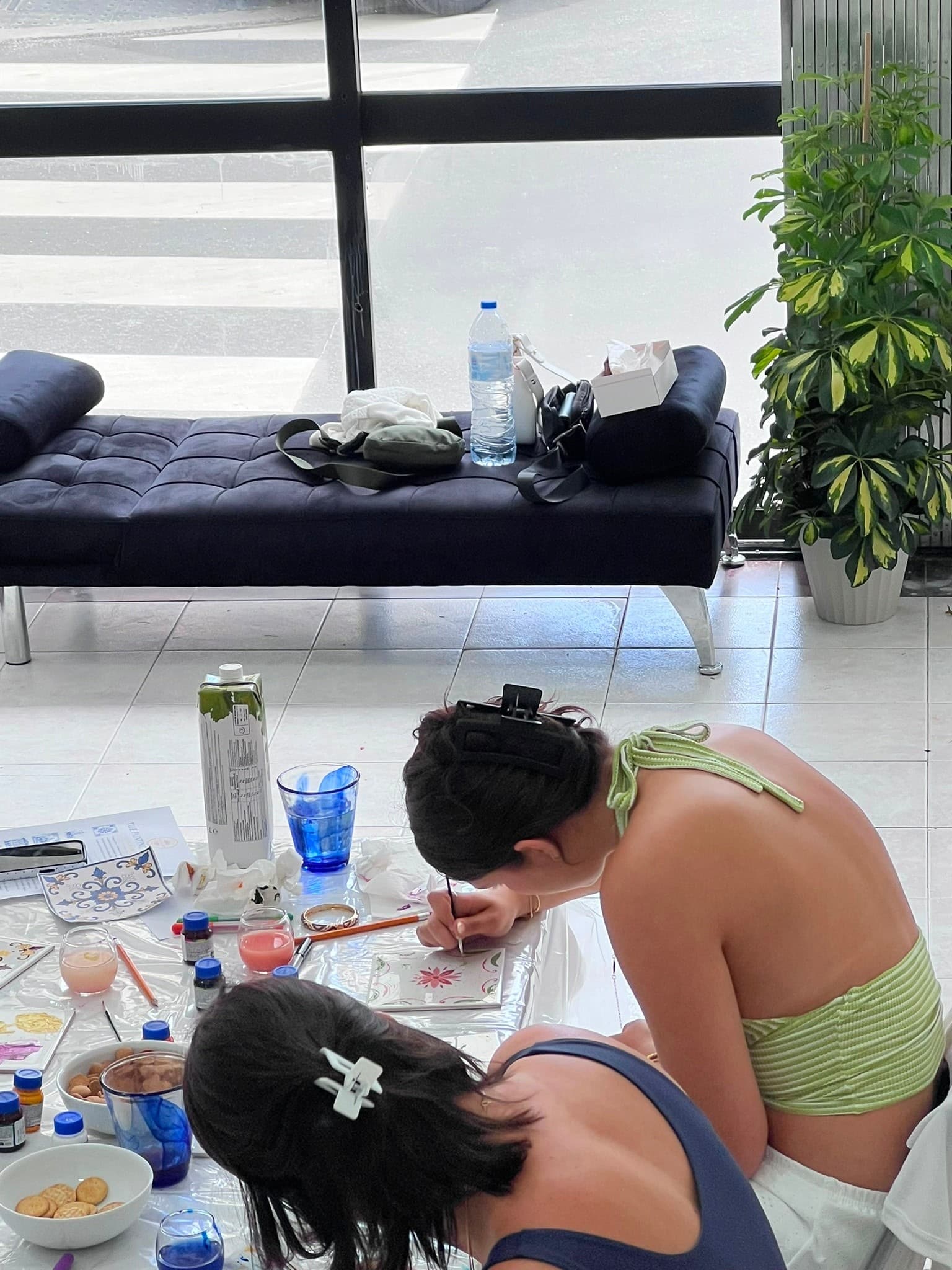 Participants painting ceramic tiles near large window in studio