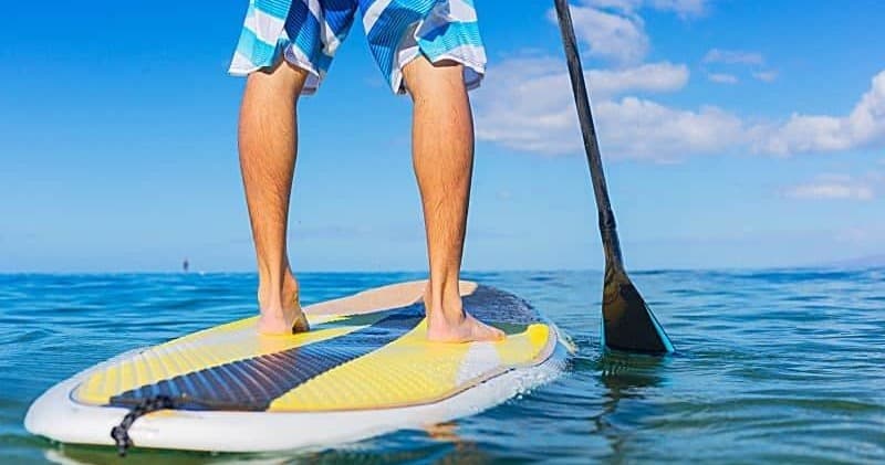 Stand-up paddleboarder feet on board in clear tropical sea