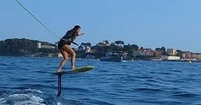 Person e-foiling over blue sea with coastal town in background