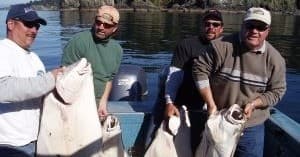 Group of anglers displaying halibut on small fishing boat in coastal waters