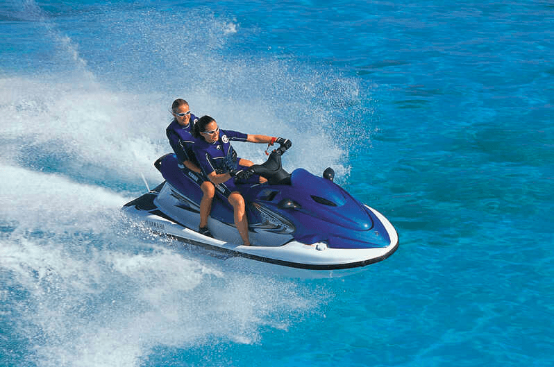 Two people riding jet ski splashing turquoise coastal waters