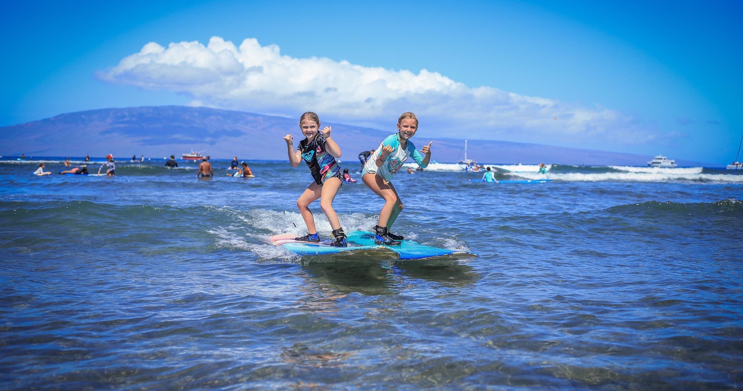 Two surfers tandem surfing in shallow reef with mountain view