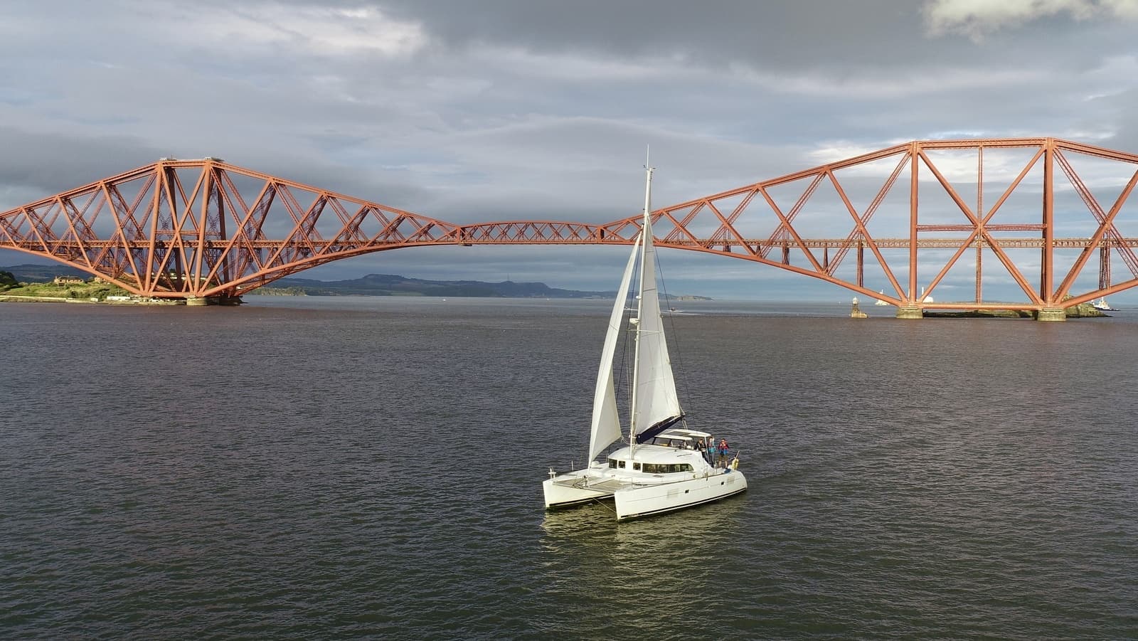Sailboat cruising near red Forth Bridge, open sea sailing