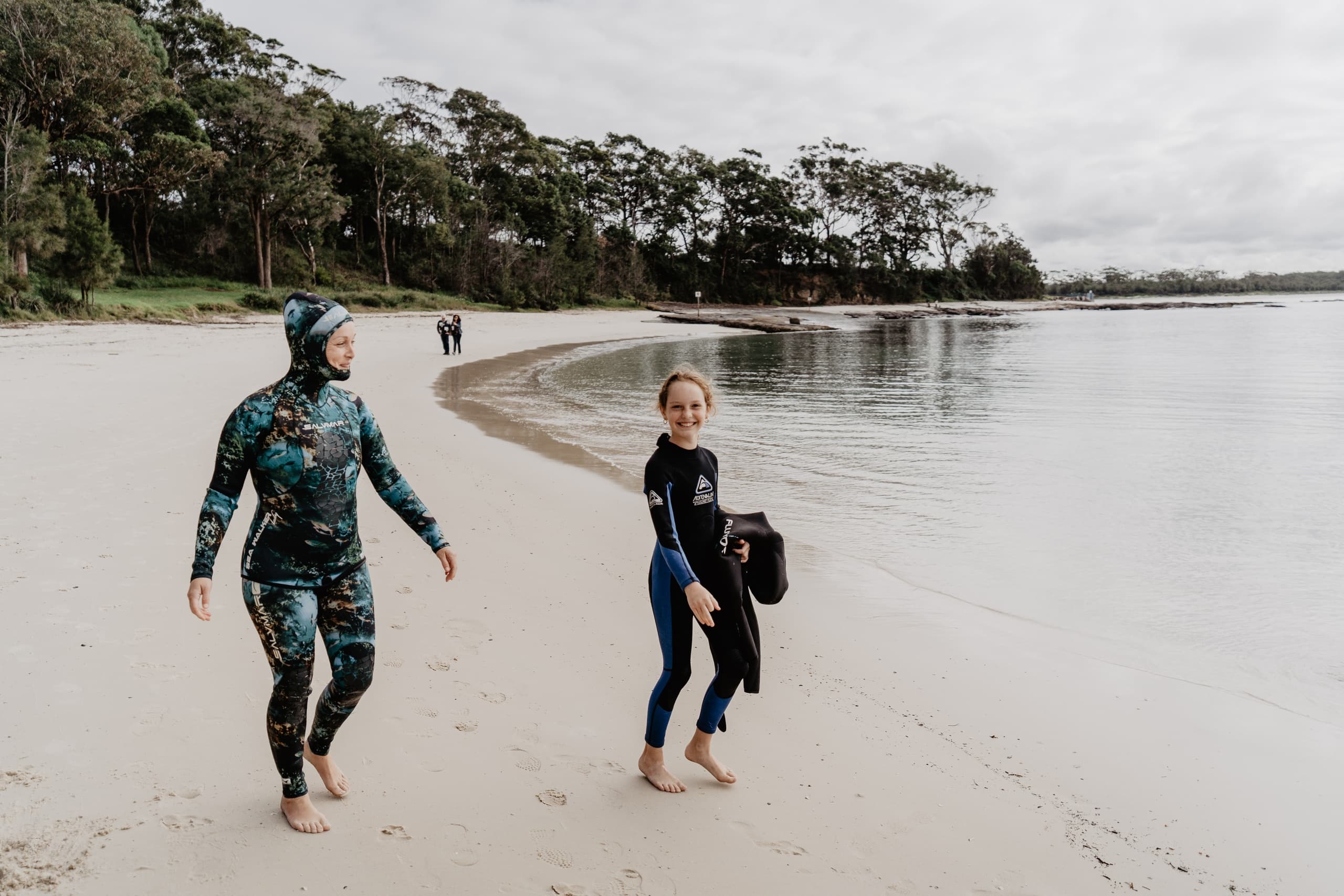 Wetsuit divers walking along remote sandy beach at low tide