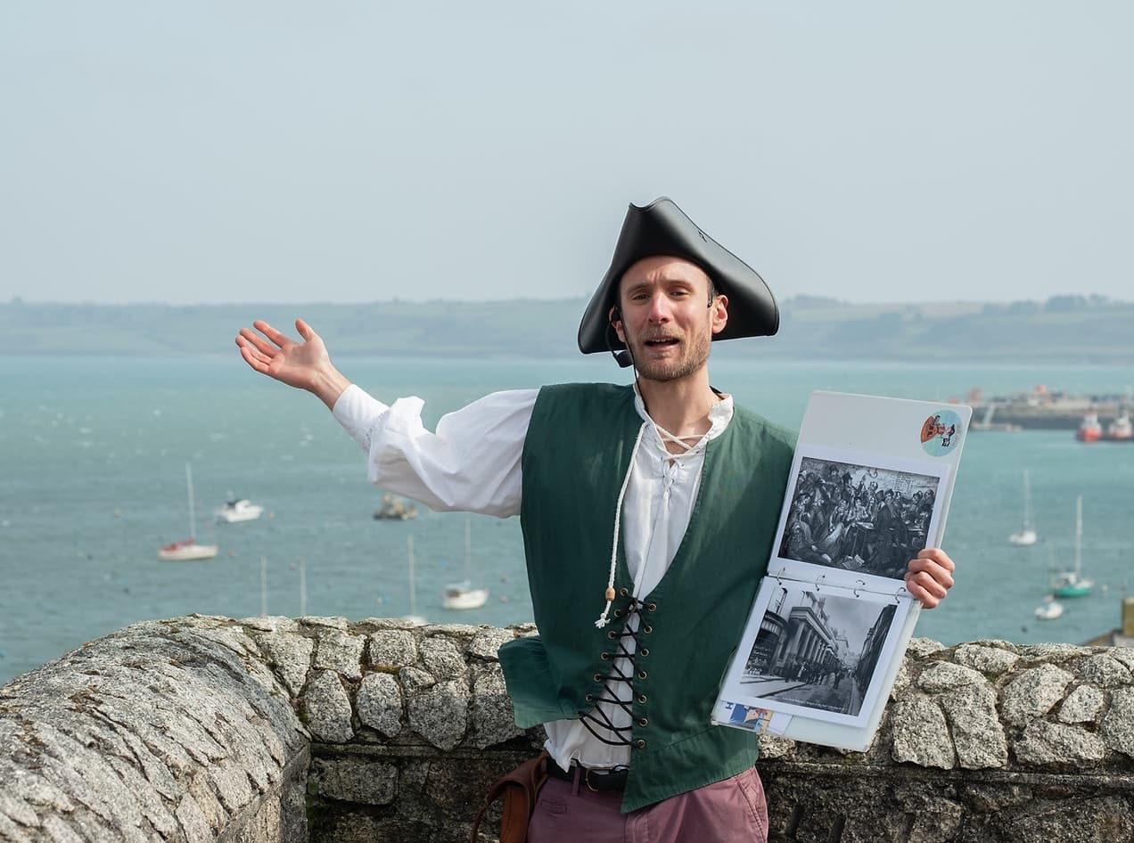 Historical guide in tricorn hat presenting Falmouth coastal vista