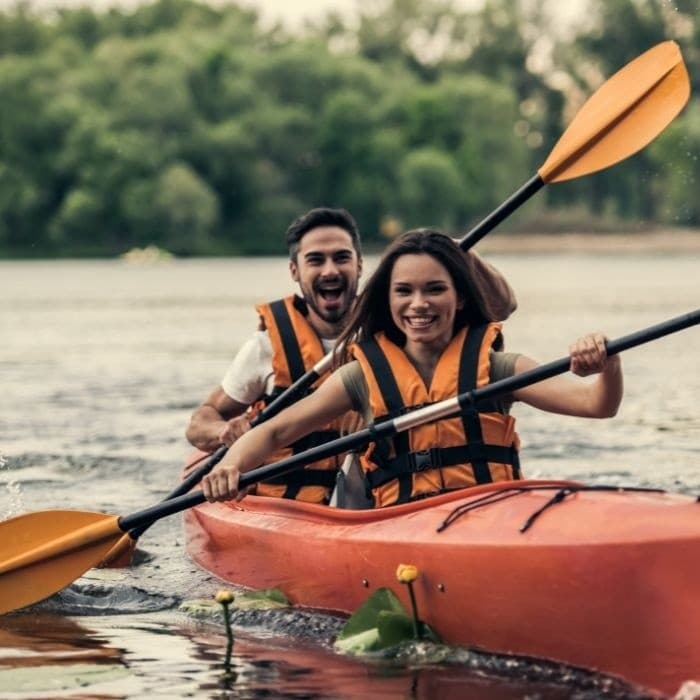 Couple kayaking tandem on river wearing life jackets, paddling