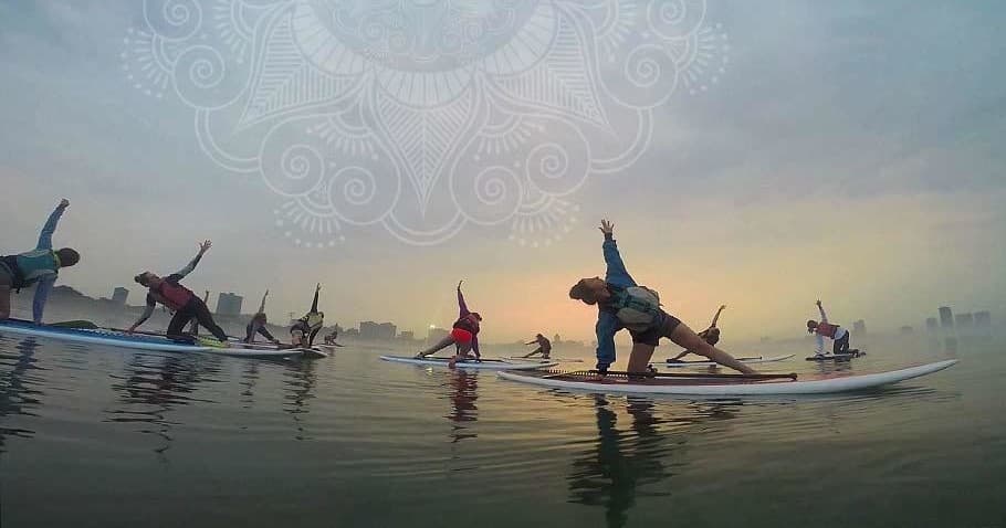 Sunrise group SUP yoga on calm water with skyline backdrop