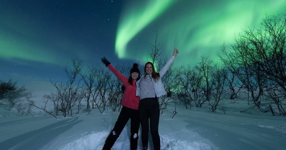 Group celebrating under vivid northern lights in snowy forest