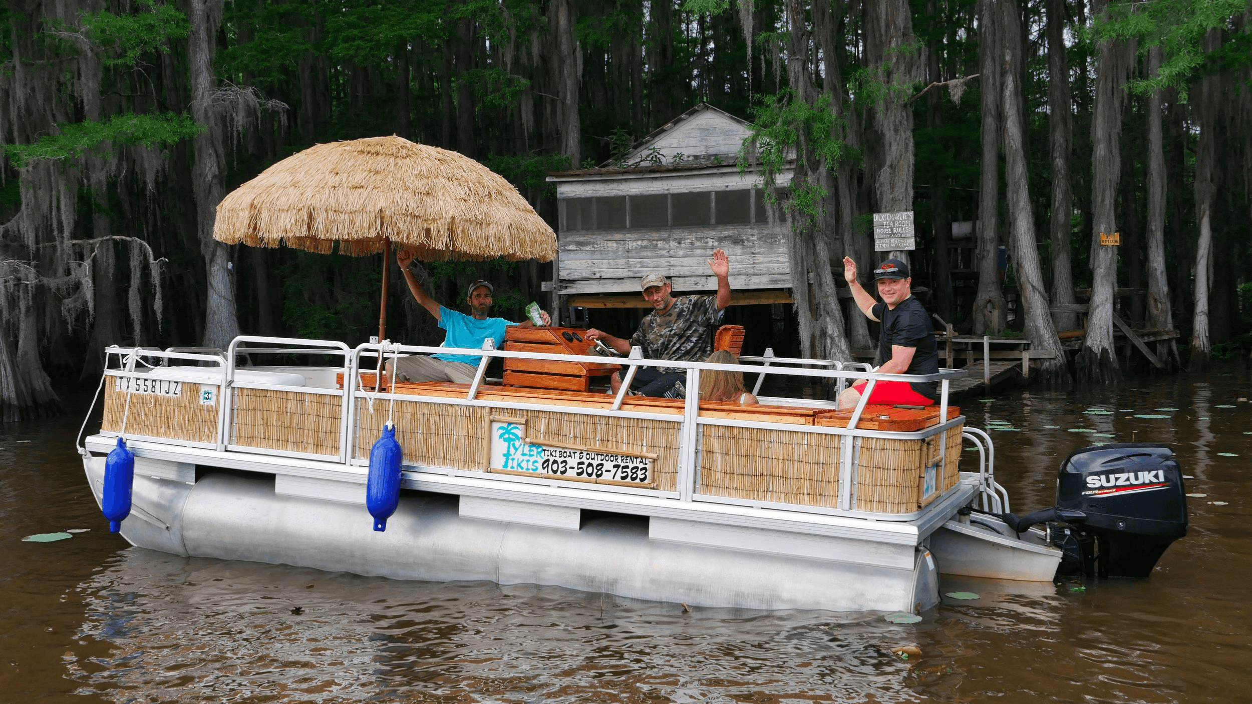 Tiki pontoon boat cruising cypress swamp with passengers waving