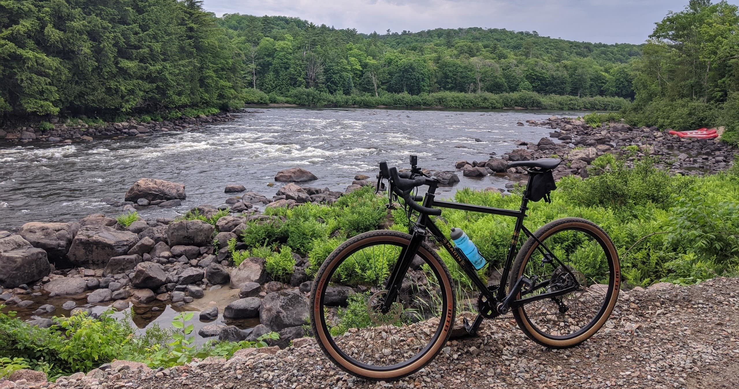 Gravel bike parked by rocky river rapids and forest shore