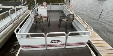 White pontoon stern tied to dock on calm lake, quiet boating spot