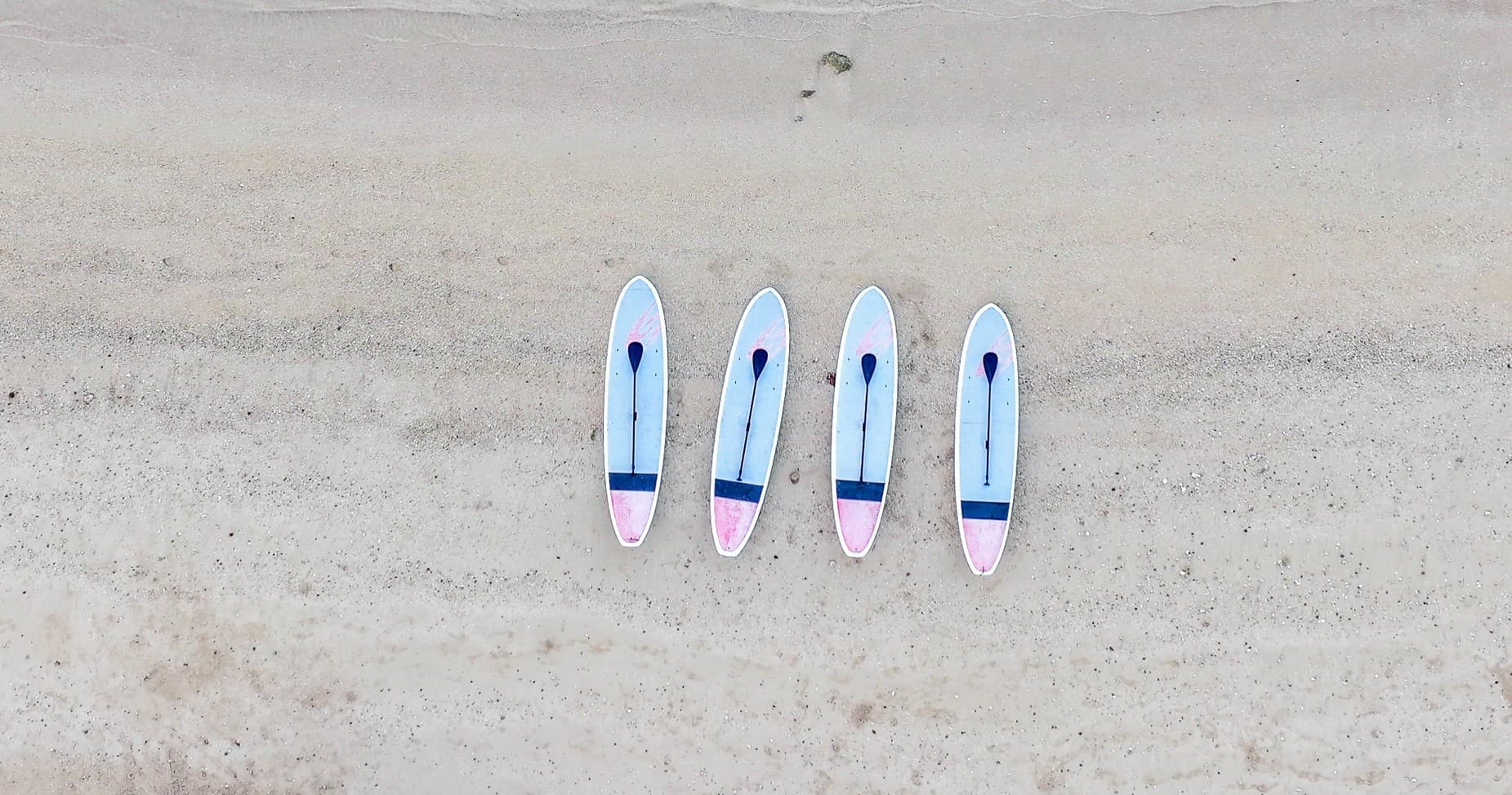 Aerial view of four surfboards lined on sandy Kauai beach