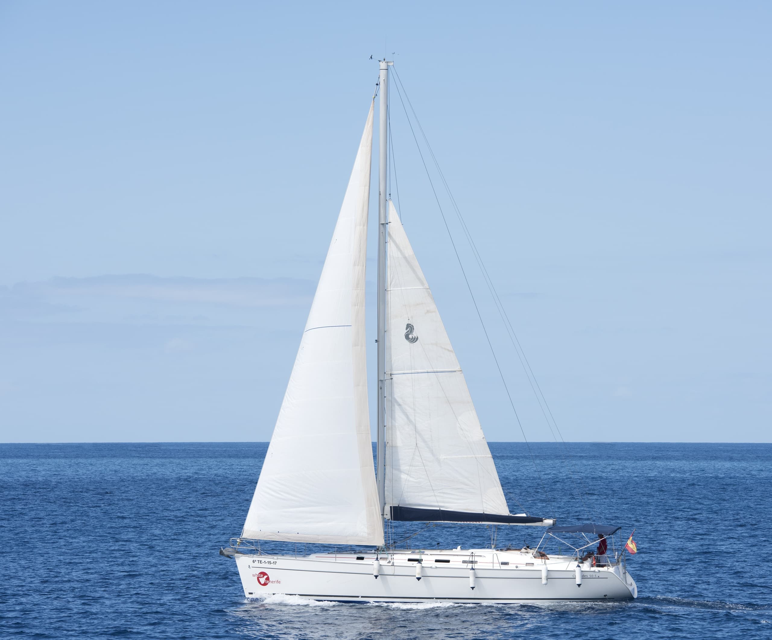 White sailboat sailing calm blue sea off Tenerife coastline