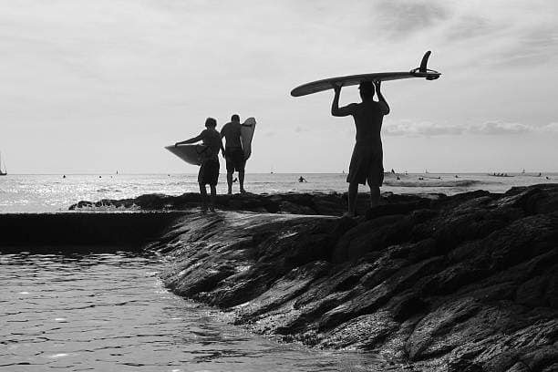 Surfers carrying boards along rocky shoreline at oceanfront