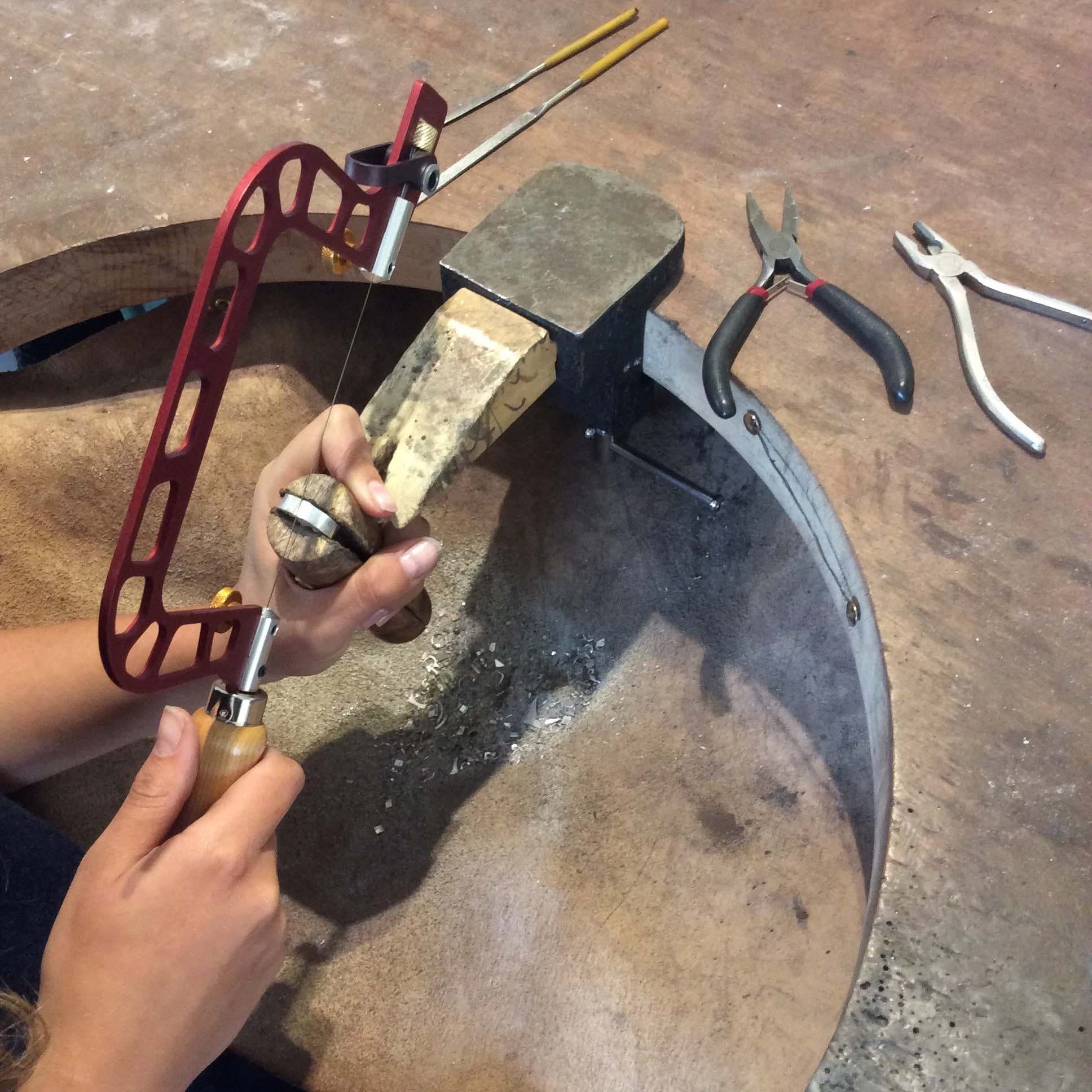 Jeweler sawing metal on a bench with hand tools indoors