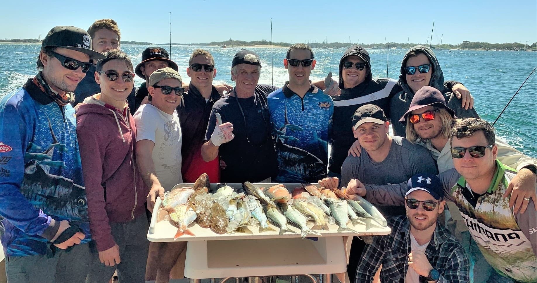 Large group with fresh catch posed on deck near coastal harbor