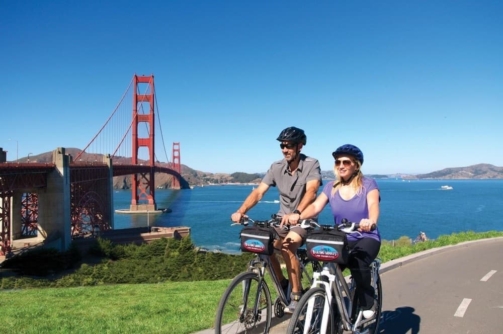 Two cyclists riding past Golden Gate with warning sign on road
