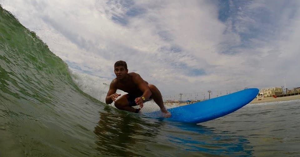 Surfer crouching on blue board riding a beach wave, sunny sky