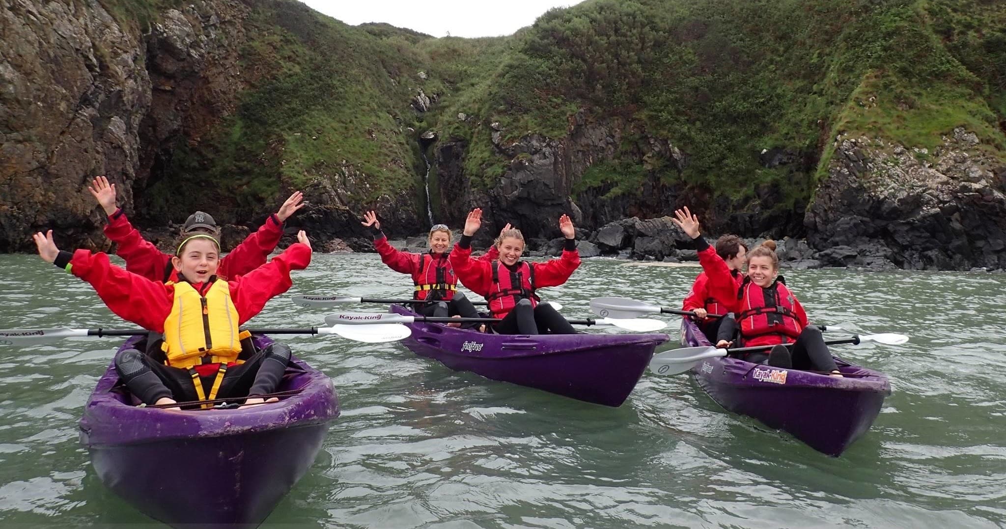 Guide-led sea kayakers paddling past rugged coastal cliffs