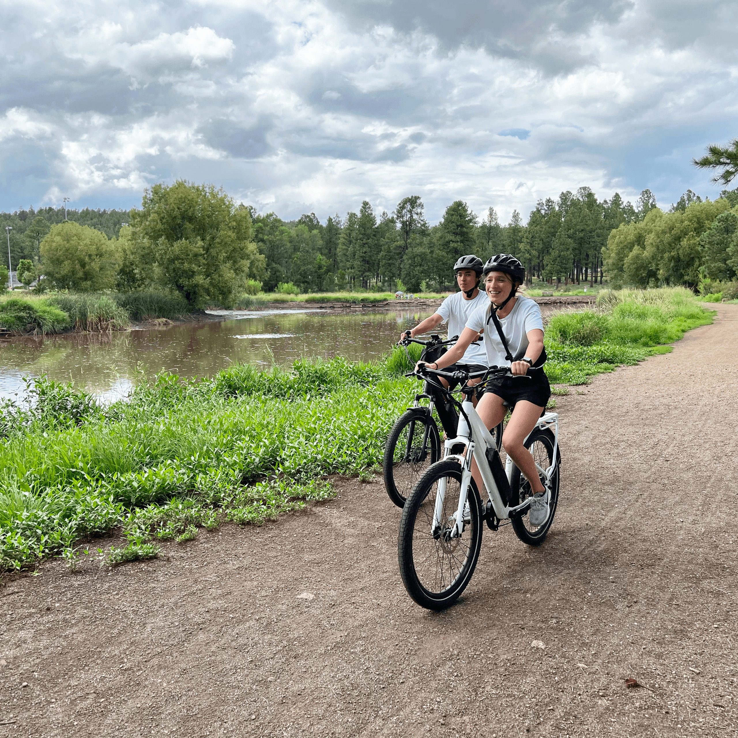 Two cyclists riding riverside trail beside green wetlands
