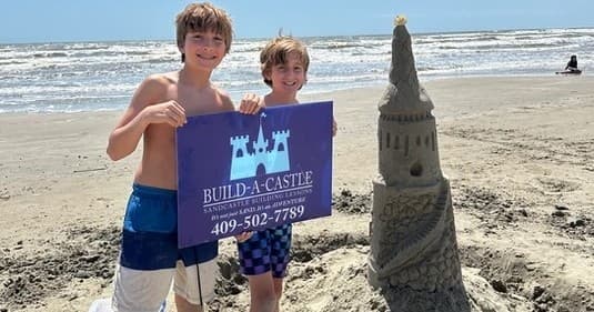 Kids posing with sandcastle and sign on Galveston beach