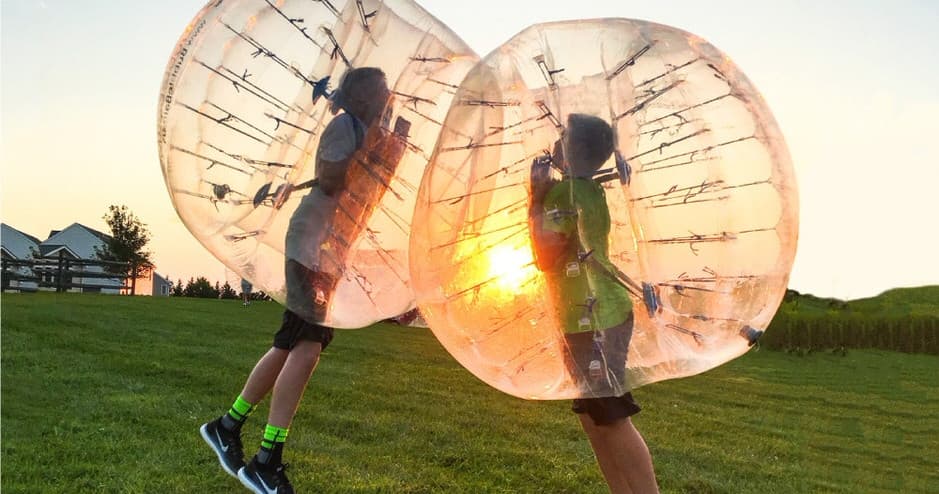 Two players colliding in zorb balls on grassy field at sunset