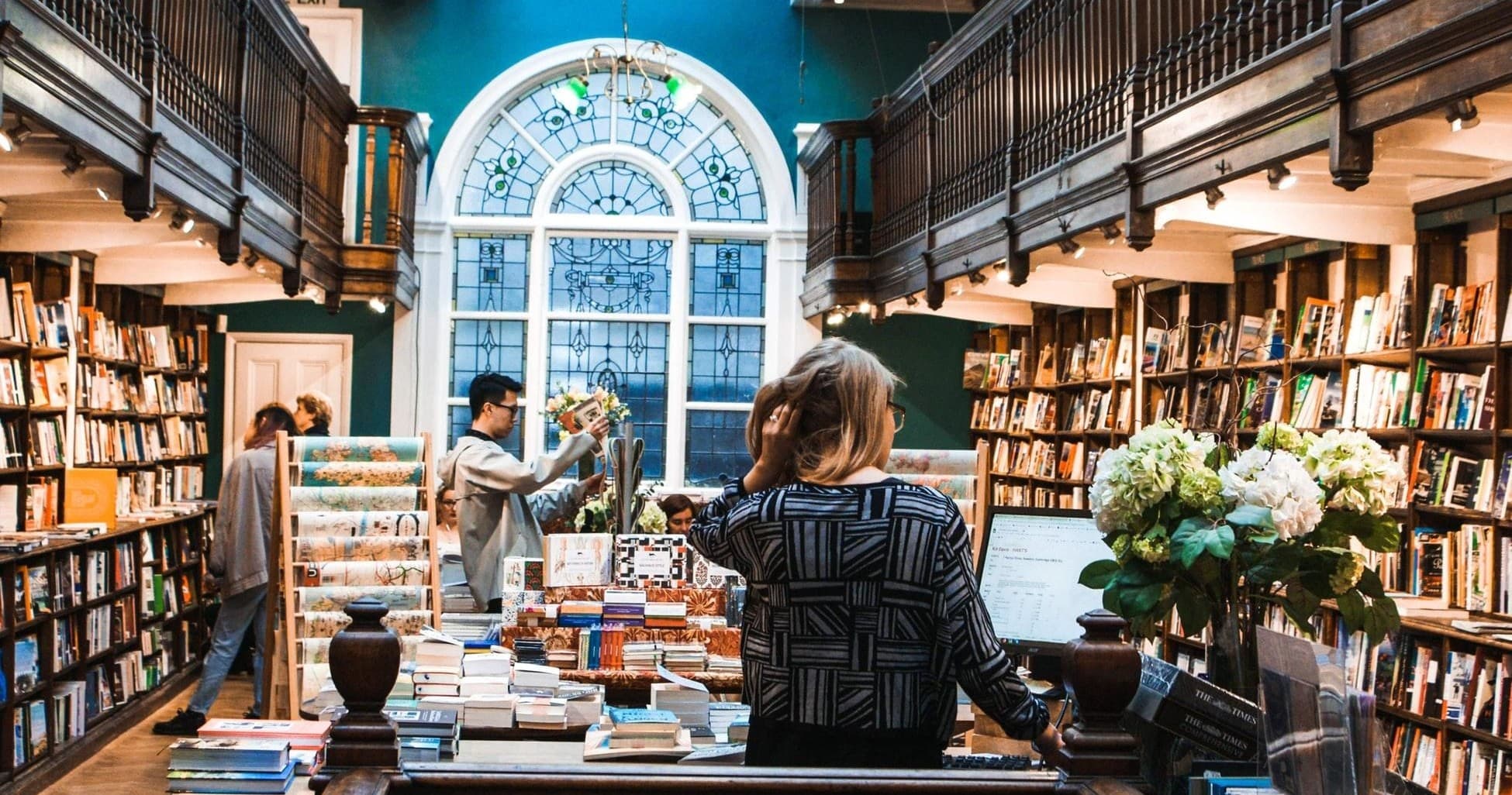 Cozy independent bookstore interior with customers browsing under arched window