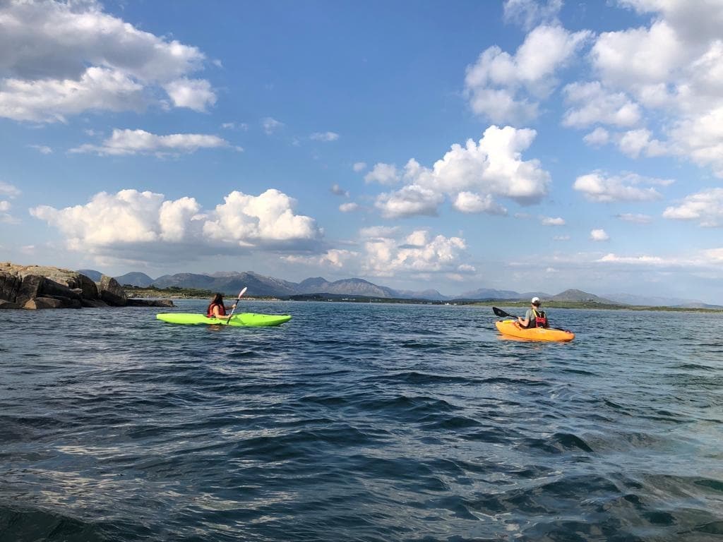 Two kayakers paddling coastal waters under blue sky clouds