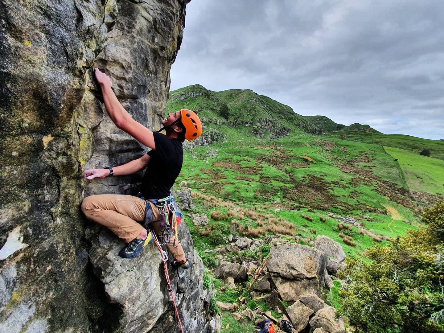 Climber scaling outdoor crag with green hills backdrop in UK