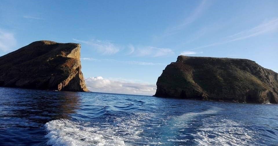 Boat approaching rocky Azores sea stacks under blue sky