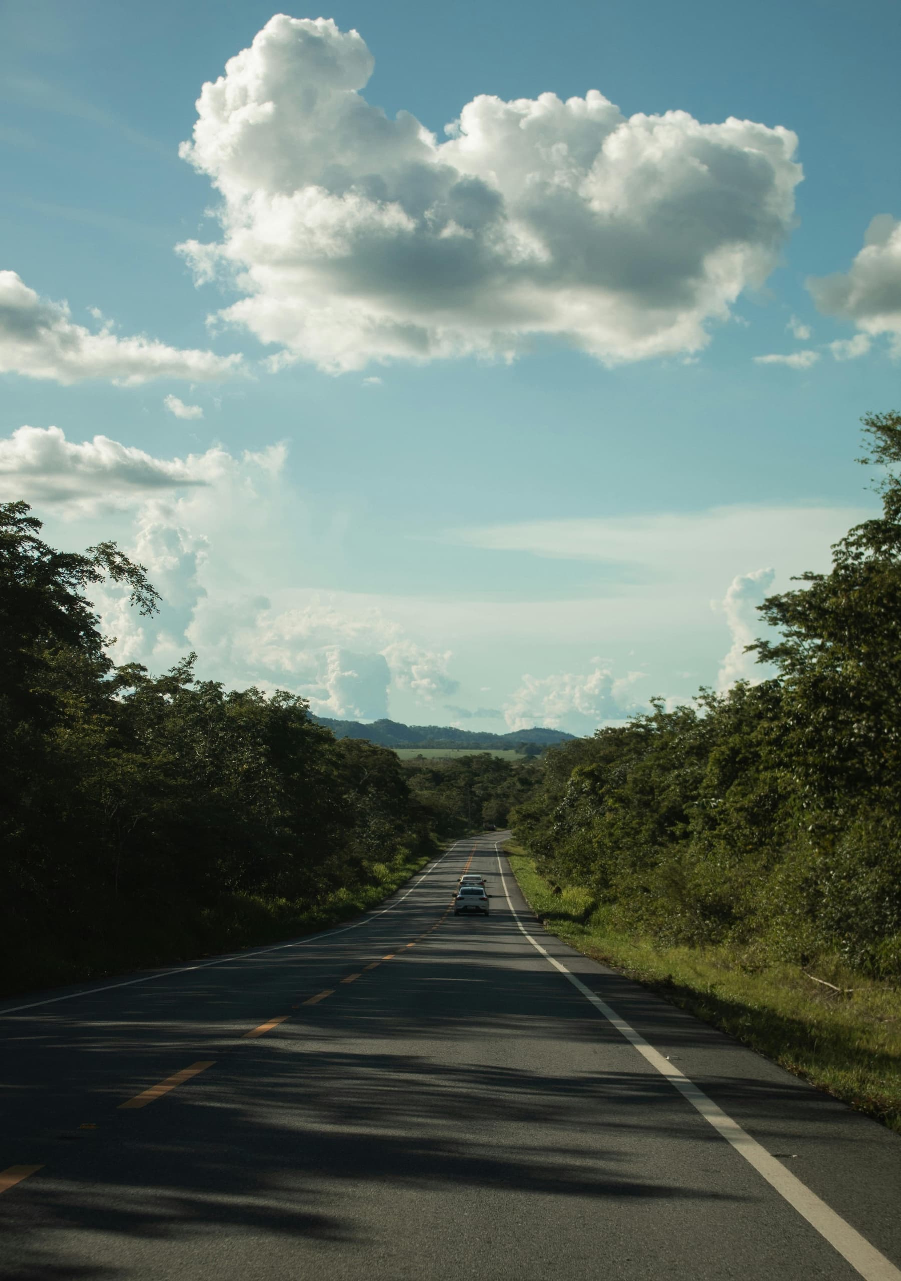 Open road through green hills under dramatic clouds, scenic drive