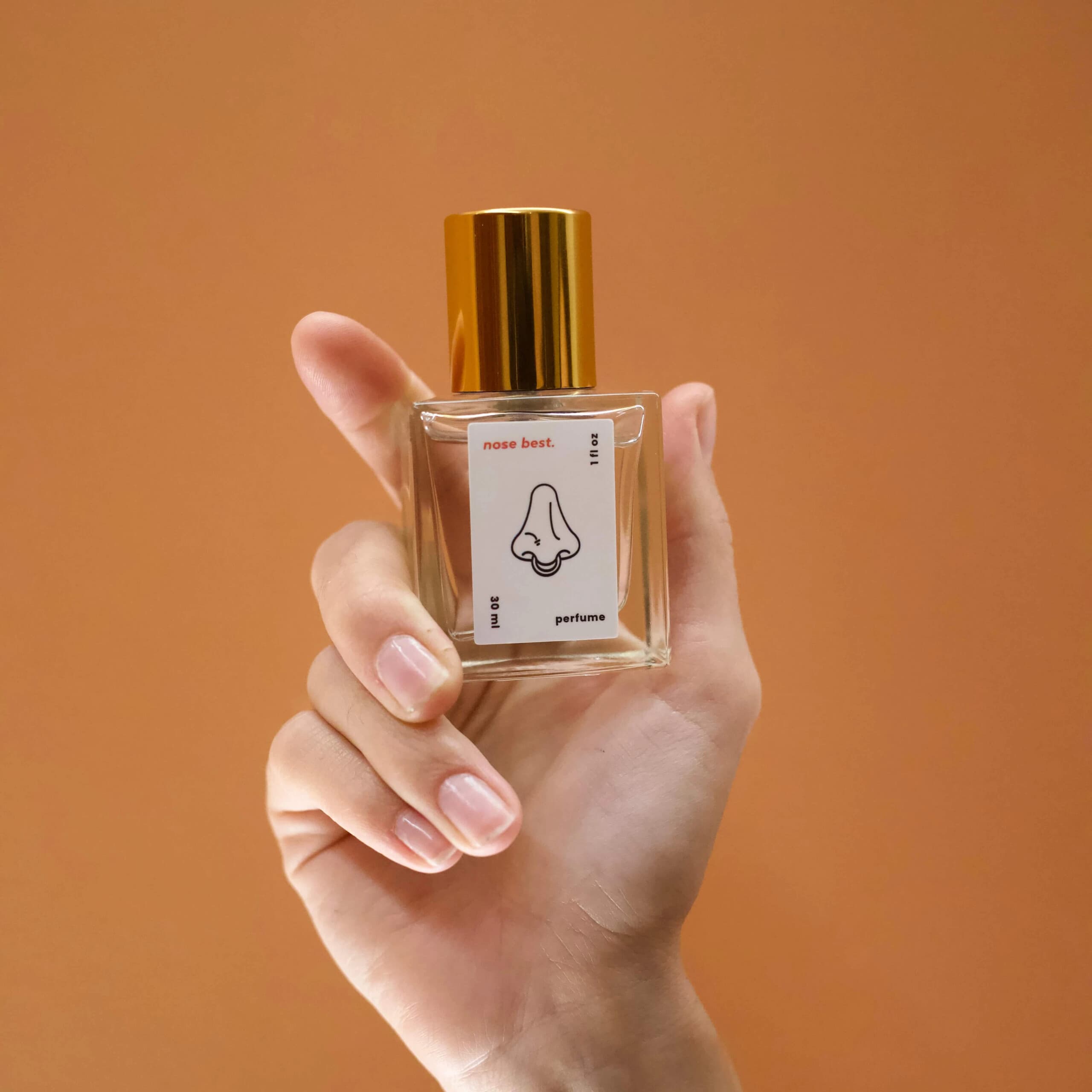 Hand holding perfume bottle against warm backdrop, product shot