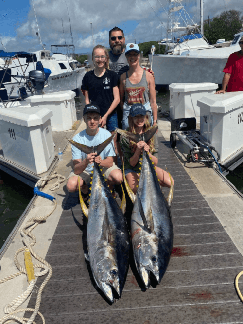 Family showcasing twin yellowfin tuna at marina after fishing