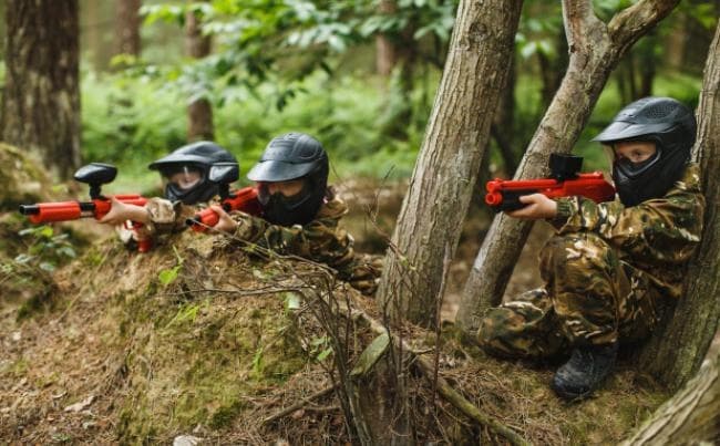Camouflaged players crouched aiming paintball markers in forest