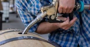 Brewer tapping oak barrel during craft beer aging process