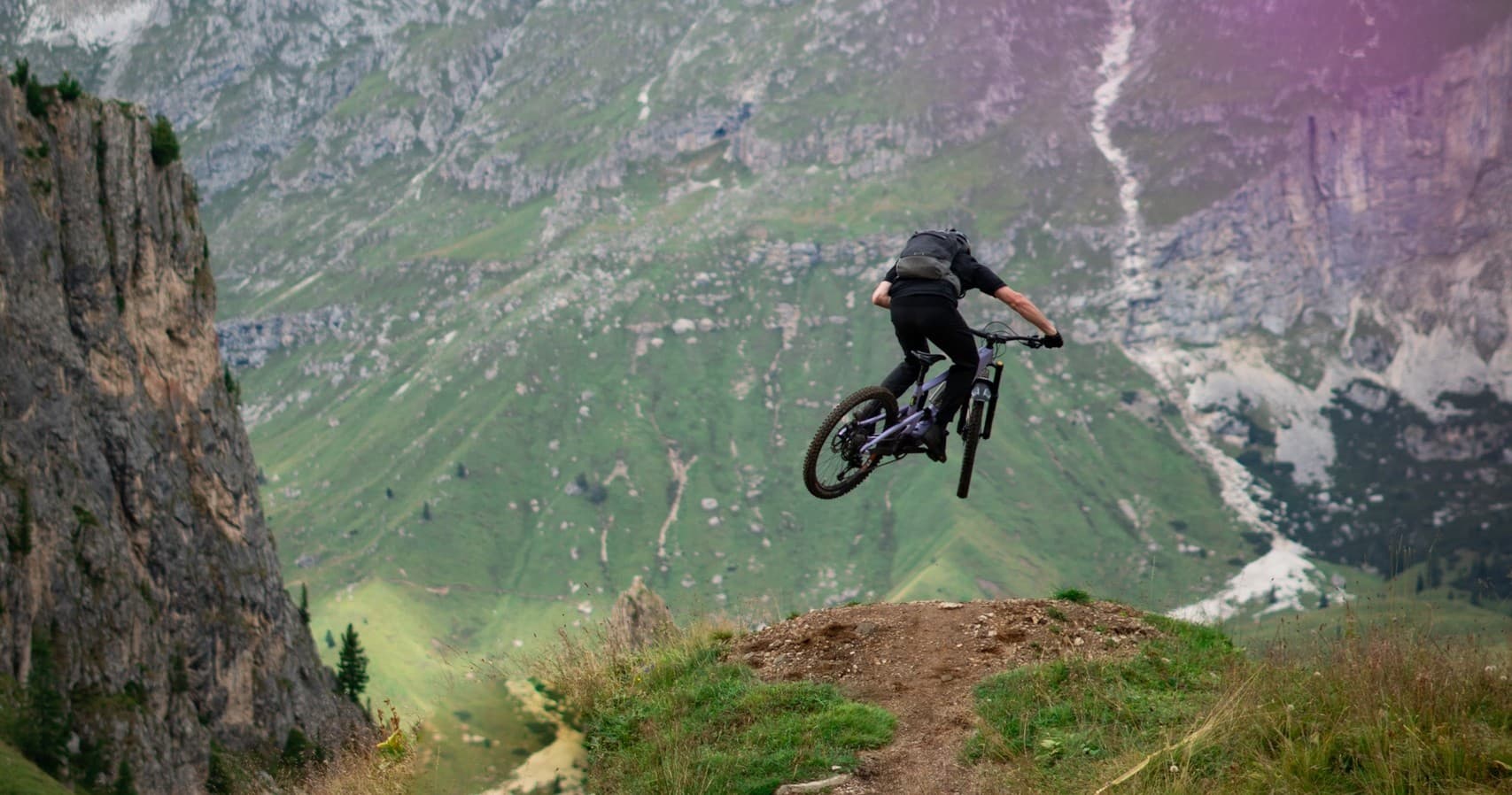 Mountain biker jumping over alpine ridge in Dolomites valley